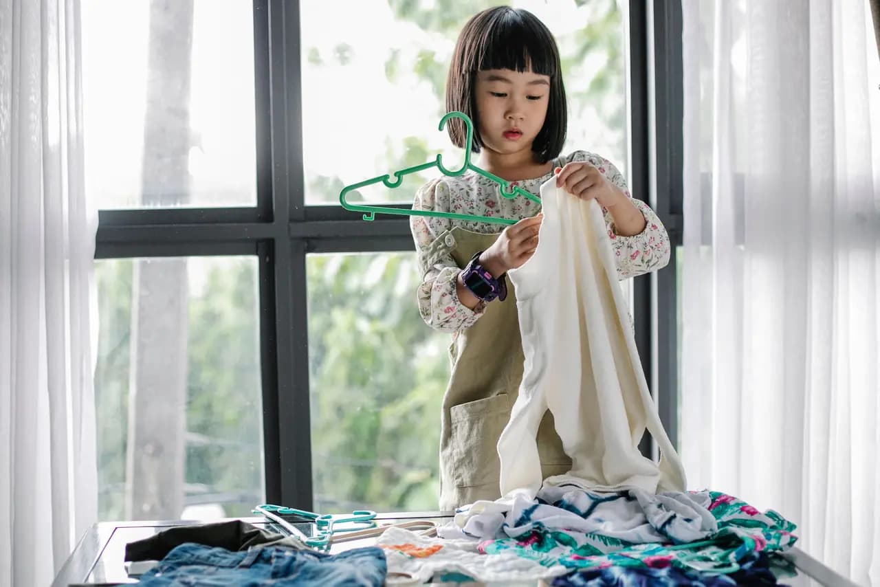 A girl hanging laundry on a hanger beside a window