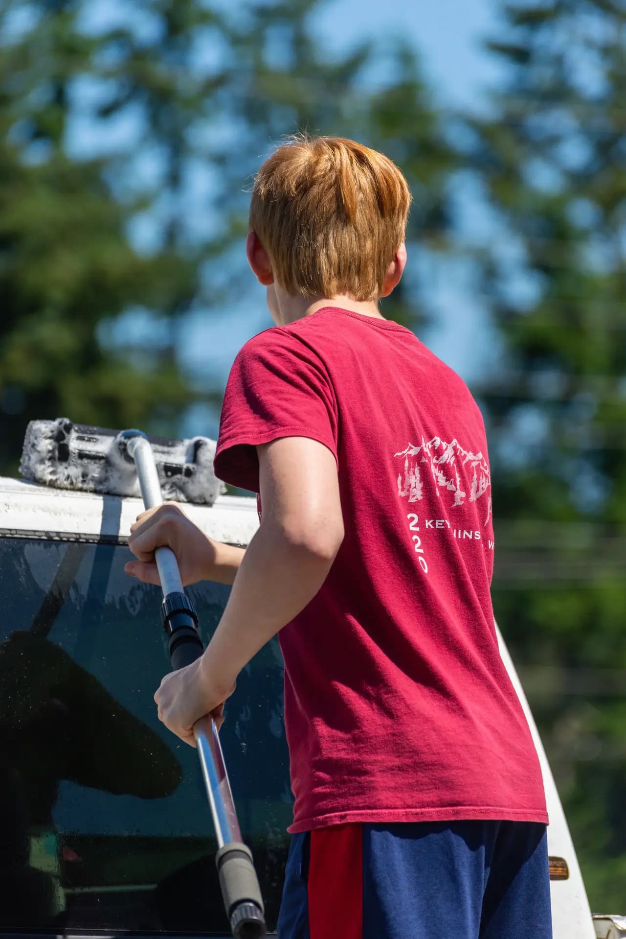 A boy in a red shirt washing a car with a hose
